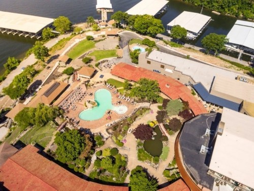 Aerial view of a resort featuring a pool, landscaped gardens, and nearby water with boat docks.