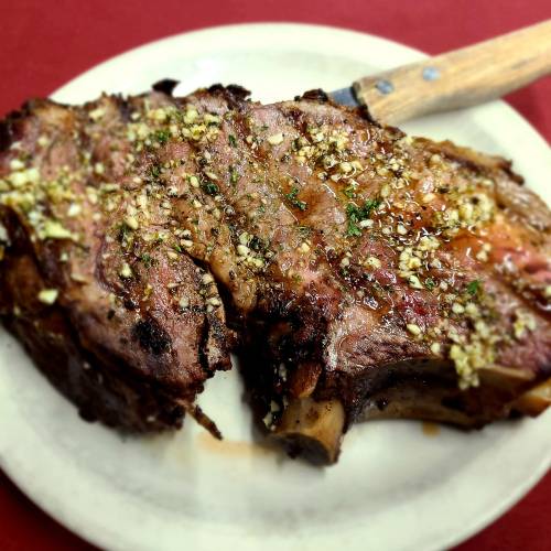 A juicy, grilled ribeye steak topped with garlic and herbs, served on a white plate with a wooden-handled knife.