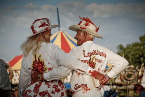 A couple in matching lobster-themed outfits smiles at a festival, with a colorful tent in the background.