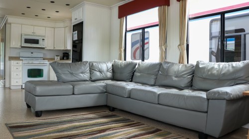 A cozy living area featuring a gray leather sectional sofa and a kitchen with modern appliances in a bright space.