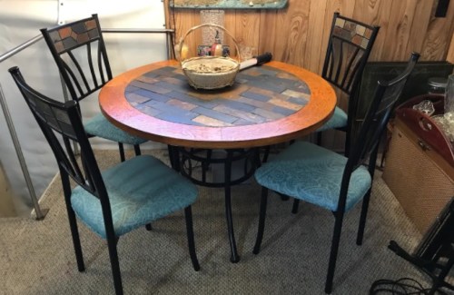 A round dining table with a stone inlay, surrounded by four black metal chairs with blue cushions.