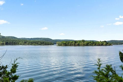 A serene lake surrounded by green hills and trees under a clear blue sky. Gentle ripples on the water's surface.