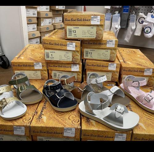 A display of various sandals in different colors and styles, stacked on boxes with size labels.