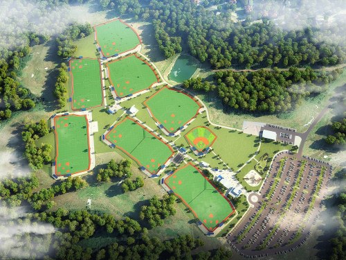 Aerial view of multiple sports fields surrounded by trees, with a large parking area nearby.