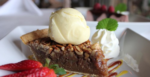 A slice of pecan pie topped with vanilla ice cream, whipped cream, and fresh strawberries on a white plate.