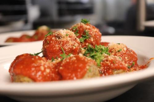 A plate of meatballs topped with marinara sauce, grated cheese, and fresh parsley.