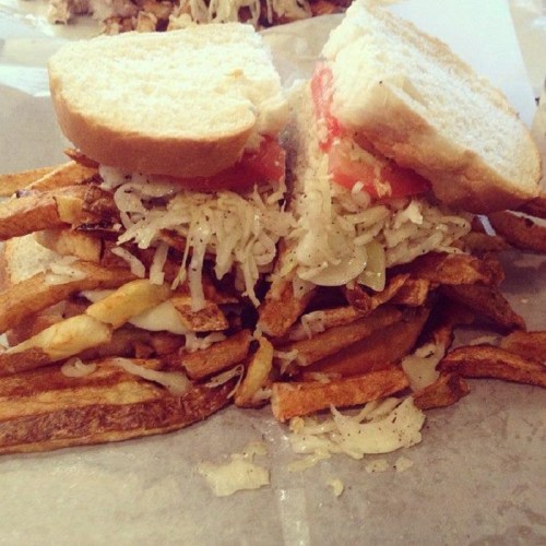 A sandwich with two slices of bread filled with fries, sauerkraut, onions, and tomato, served on a paper-lined plate.