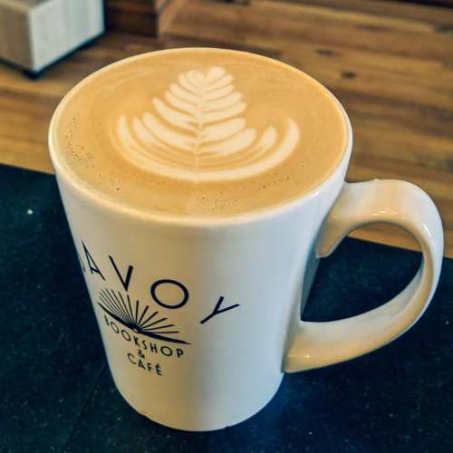 A latte in a white mug with a leaf design on top, placed on a dark countertop.