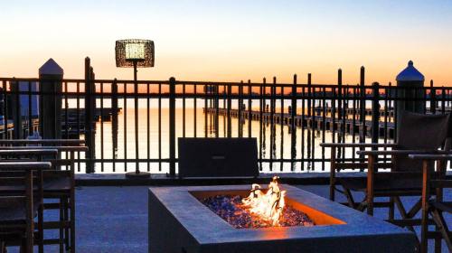 A serene waterfront scene at sunset, featuring a fire pit, chairs, and a lamp by a calm waterway with docks.