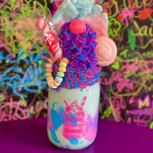 A colorful milkshake topped with candy, sprinkles, and cotton candy, set against a vibrant graffiti background.