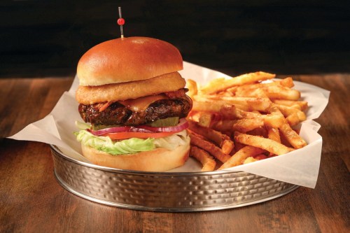 A juicy burger with onion rings, lettuce, and pickles, served with a side of crispy French fries on a metal tray.