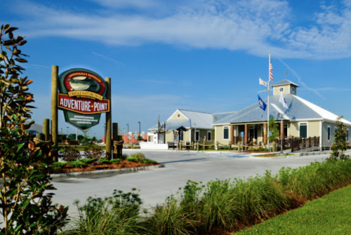 A building with a sign reading "Adventure Point," surrounded by greenery and a clear blue sky.