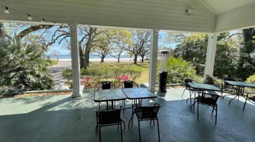 View from a porch with tables and chairs overlooking a scenic landscape with trees and a body of water in the distance.