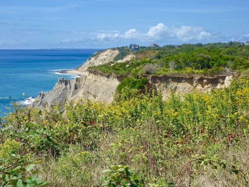 Coastal landscape featuring cliffs, lush greenery, and a serene blue ocean under a clear sky.