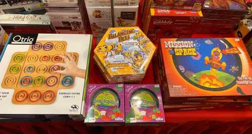 A display of board games, including "Otrio," "Bumbling Bees," and "Mission to Space," on a red tablecloth.