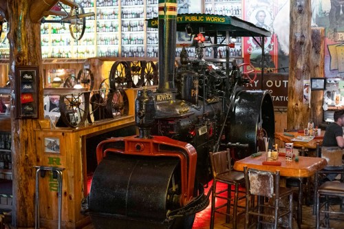 A vintage steam engine displayed in a rustic restaurant, surrounded by wooden decor and tables.