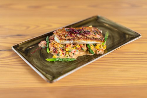 A beautifully plated dish featuring seared fish atop a colorful vegetable medley with asparagus and a creamy sauce.