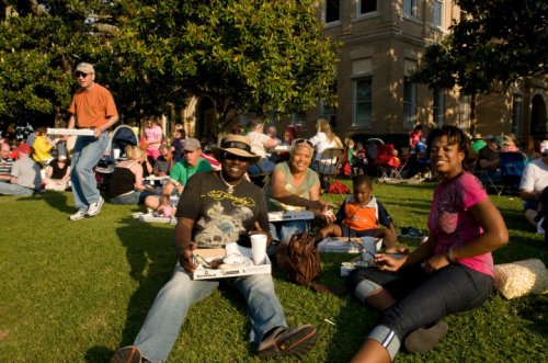 A group of people enjoying a picnic on the grass, smiling and relaxing in a sunny outdoor setting.