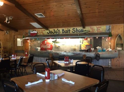 Interior of JoJo's Bait Shop featuring wooden decor, tables, and a display area with fishing gear and a canoe.