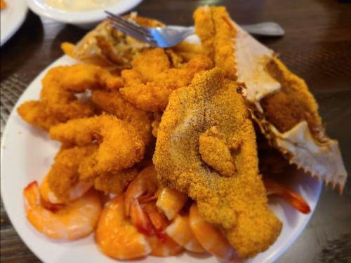 A plate of fried seafood, including shrimp, fish fillets, and crab, all coated in a golden breading.