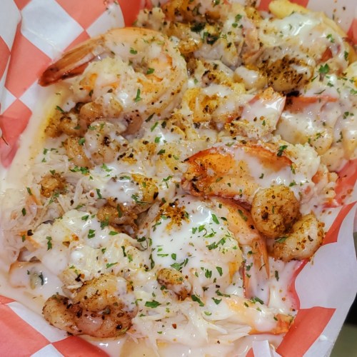 A close-up of a seafood dish featuring shrimp, rice, and melted cheese, garnished with herbs in a red and white basket.