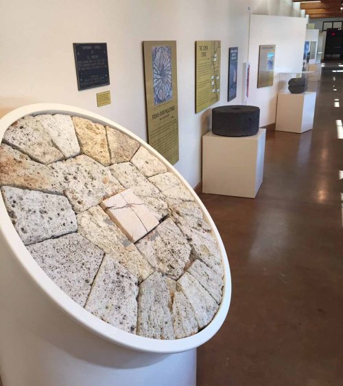 A circular stone display with various textures, surrounded by informational plaques in a well-lit gallery.