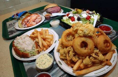 A tray of food featuring onion rings, fries, a seafood sandwich, a salad, and a roast beef sandwich.