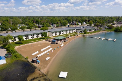 Aerial view of a beach with lounge chairs, a hotel, and a calm lake under a blue sky with scattered clouds.