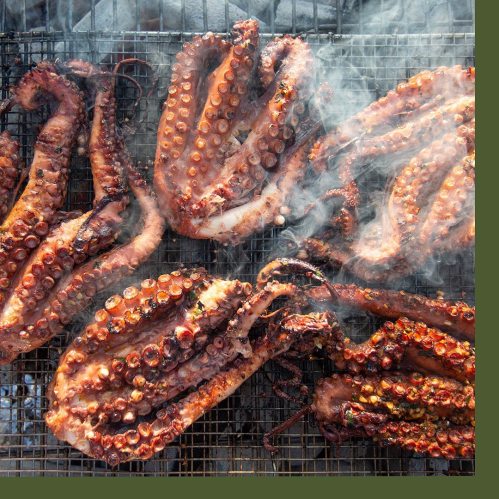 Grilled octopus tentacles on a smoky barbecue grill, showcasing a rich, charred texture.