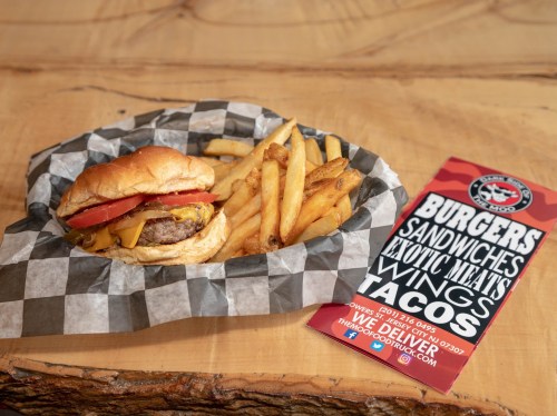 A cheeseburger with tomato and fries on a checkered plate, next to a menu featuring burgers, sandwiches, and tacos.