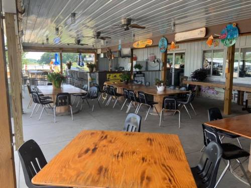 Outdoor dining area with wooden tables, black chairs, and ceiling fans, surrounded by plants and decor.