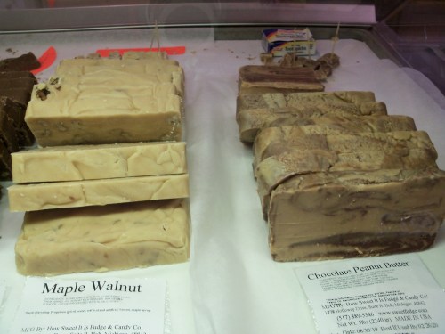 A display of fudge varieties, including Maple Walnut and Chocolate Peanut Butter, arranged on a counter.