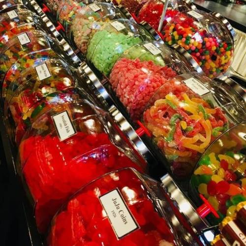 A colorful display of various candies in clear containers, including gummies, jelly beans, and sour treats.