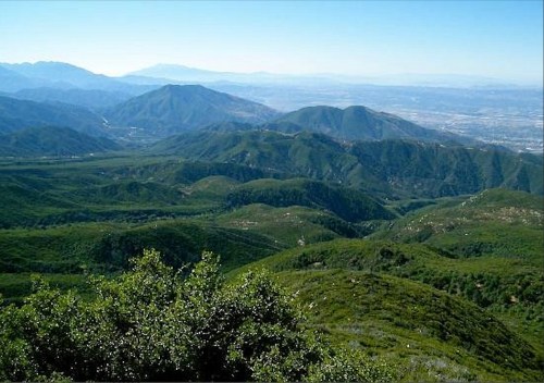 Lush green mountains stretch across the landscape under a clear blue sky, with distant peaks visible on the horizon.