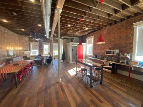 Spacious, modern loft with exposed brick walls, wooden floors, and a dining area featuring red chairs and pendant lights.