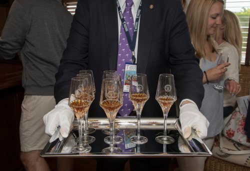 A server in a suit holds a tray of champagne glasses, with guests mingling in the background.