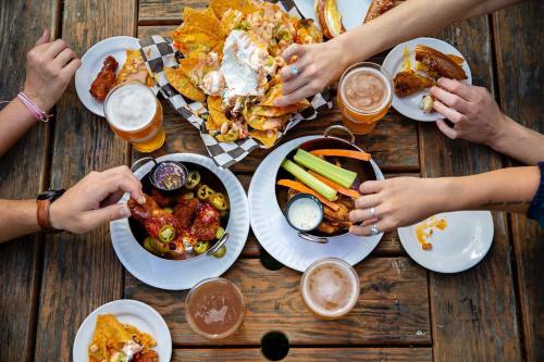 A table filled with various appetizers, including nachos, chicken wings, and drinks, with hands reaching for food.