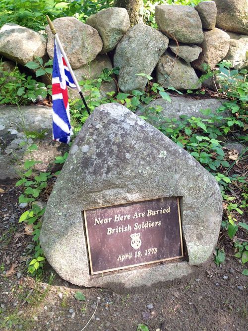 A stone marker with a plaque reading "Near Here Are Buried British Soldiers, April 19, 1775," beside a British flag.