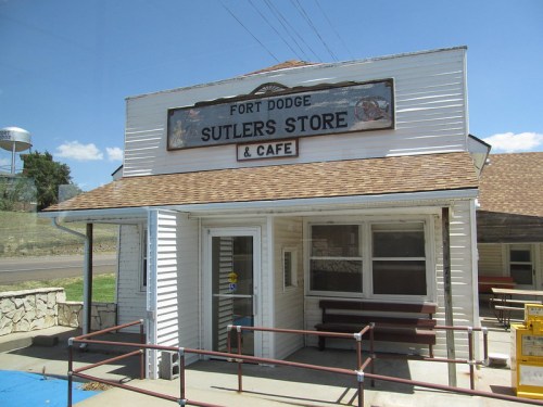 Historic building with a sign reading "Fort Dodge Sutlers Store & Cafe," featuring a porch and benches outside.