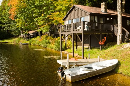 A serene lakeside scene featuring a wooden cabin, colorful autumn trees, and a small boat docked by the water.