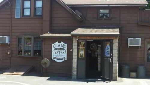 A rustic brown building with a sign reading "Clams & Oysters" at the entrance, featuring air conditioning units.