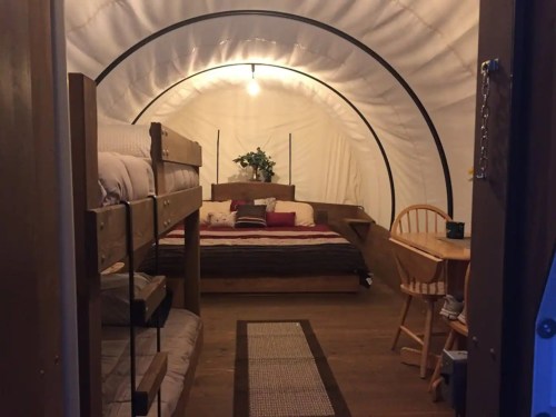 Cozy interior of a glamping tent featuring a bunk bed, a double bed, and a small dining area.