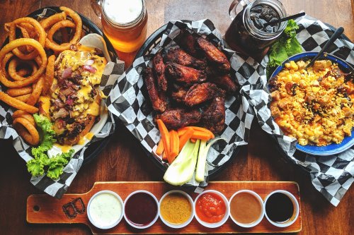 A spread of delicious food including wings, nachos, mac and cheese, onion rings, and a variety of dipping sauces.