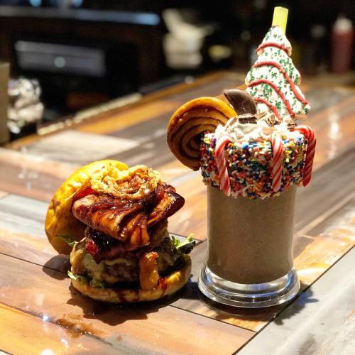 A festive burger topped with crispy onions and a colorful holiday milkshake adorned with candy canes and sprinkles.