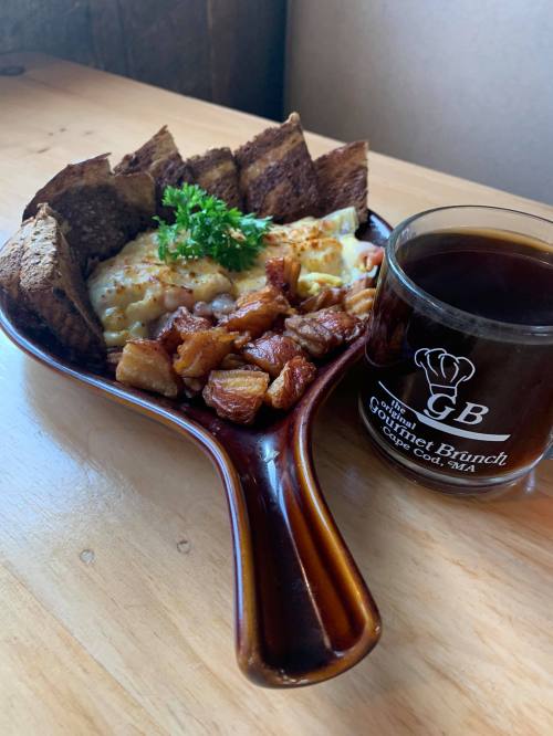 A plate of breakfast with eggs, potatoes, and toast, accompanied by a cup of coffee on a wooden table.