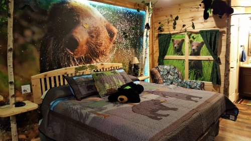 Cozy bedroom with bear-themed decor, featuring a large mural, patterned bedding, and rustic wooden furniture.