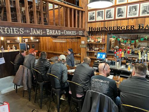 A group of people sitting at a bar with wooden decor, drinks, and a variety of bottles displayed on the shelves.