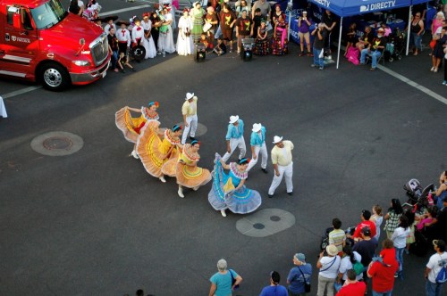A vibrant dance performance with colorful costumes, surrounded by an enthusiastic crowd and a red truck in the background.