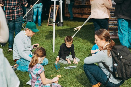 A family enjoys outdoor activities, with children playing on the grass while adults engage nearby at a festival.