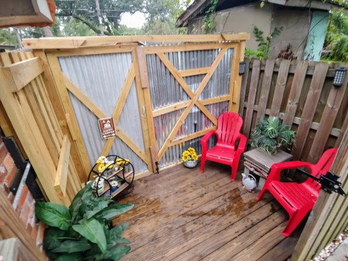 A cozy outdoor space with wooden fencing, red chairs, potted plants, and a decorative bicycle.